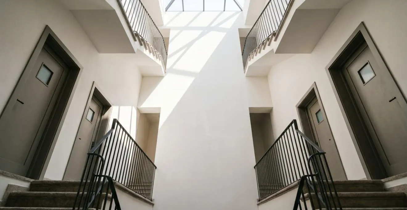 Vue grand angle d'un hall d'immeuble de rapport avec escalier central et portes d'appartements multiples